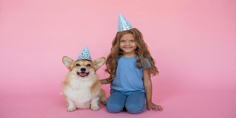 A child with a dog wearing a party hat

Description automatically generated